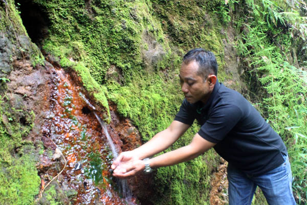 Supandi, Warga Desa Sumberbening, mencoba kesegaran air dari sumber mata air Plancuran yang keluar dari bawah bukit batu. Foto: Petrus Riski