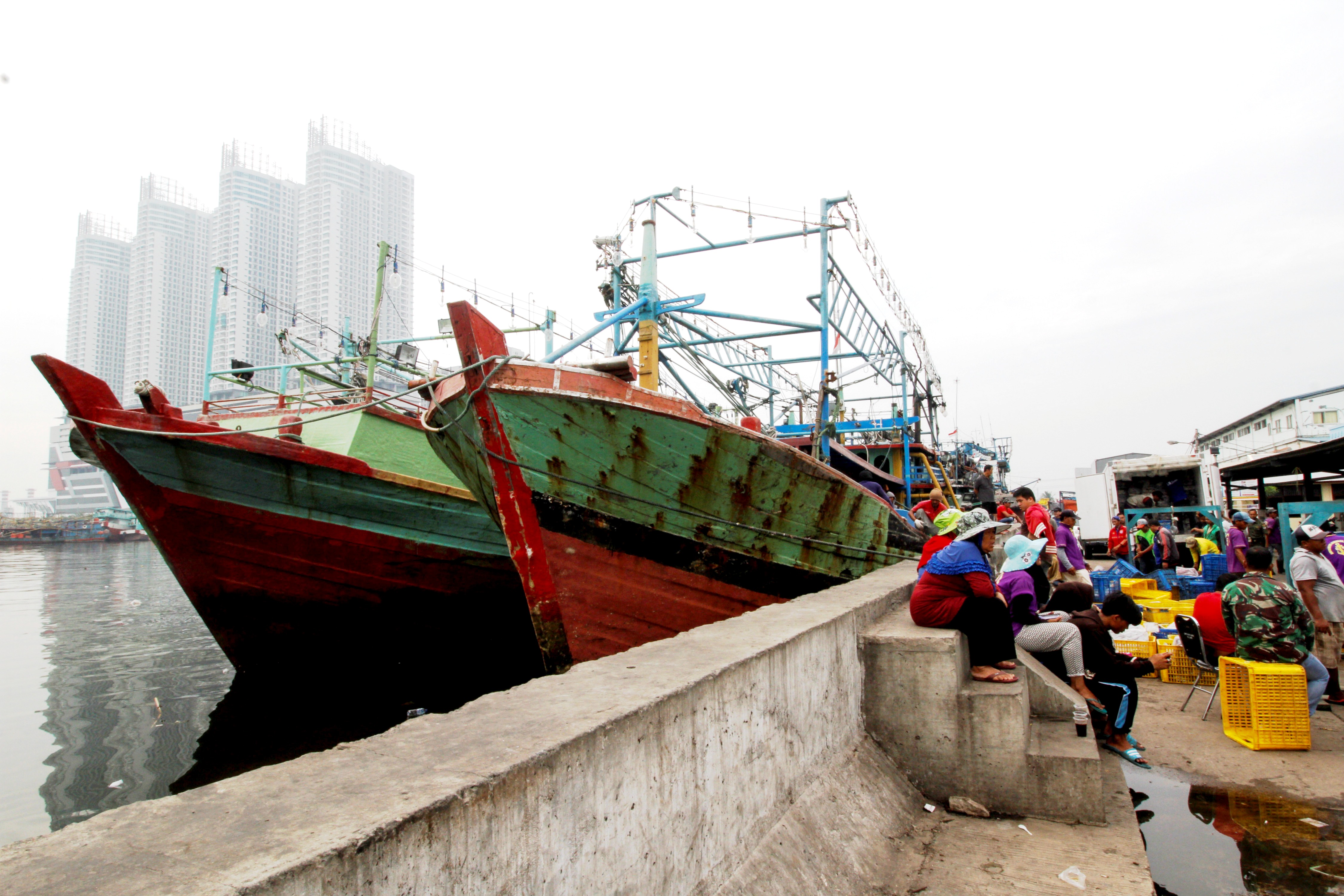 Sekelompok buruh angkut ikan sedang menunggu di dekat kapal yang bersandar di Pelabuhan Perikanan Muara Angke, Jakarta Utara pada akhir November 2016. Foto : Junaidi Hanafiah