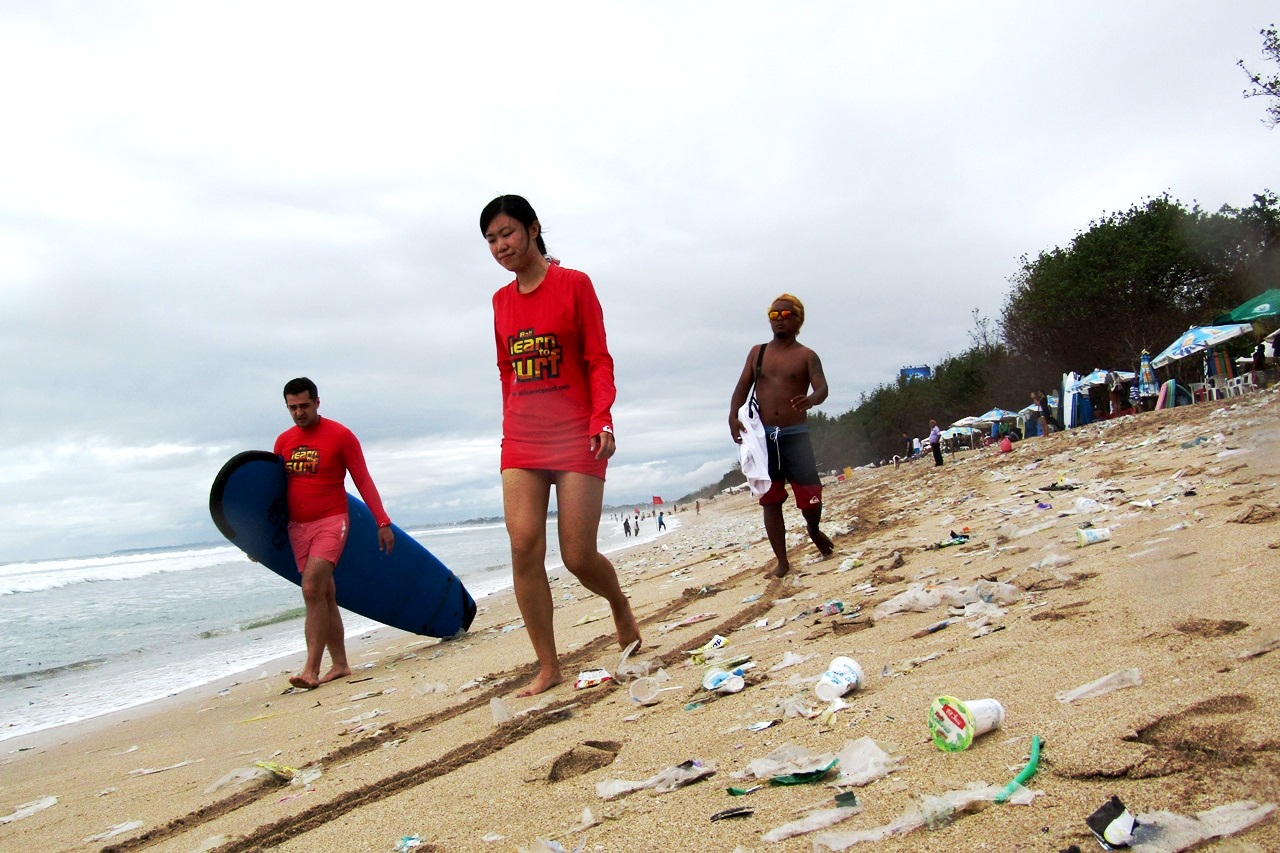 Wisatawan surfing di tengah gulungan ombak penuh sampah saat angin Barat di Pantai Kuta sampai Seminyak, Bali. Sampah di pesisir pantai menjadi masalah bagi lingkungan dan pariwisata Bali. Foto: Luh De Suriyani