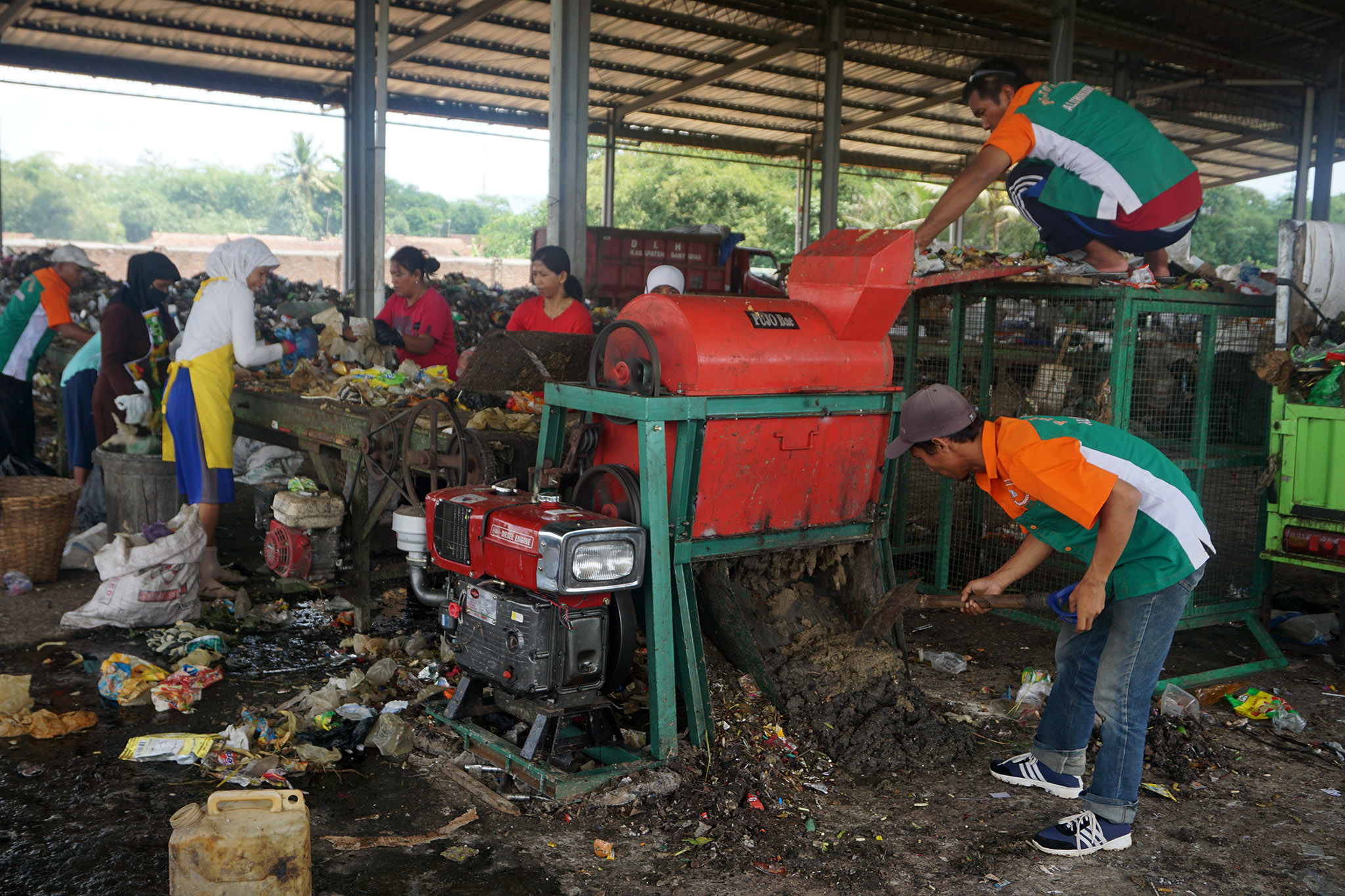 Seorang pekerja sedang mengumpulkan bubur sampah organik, sementara di sebelahnya para ibu memungut sampah plastik | Foto: L Darmawan/Mongabay Indonesia