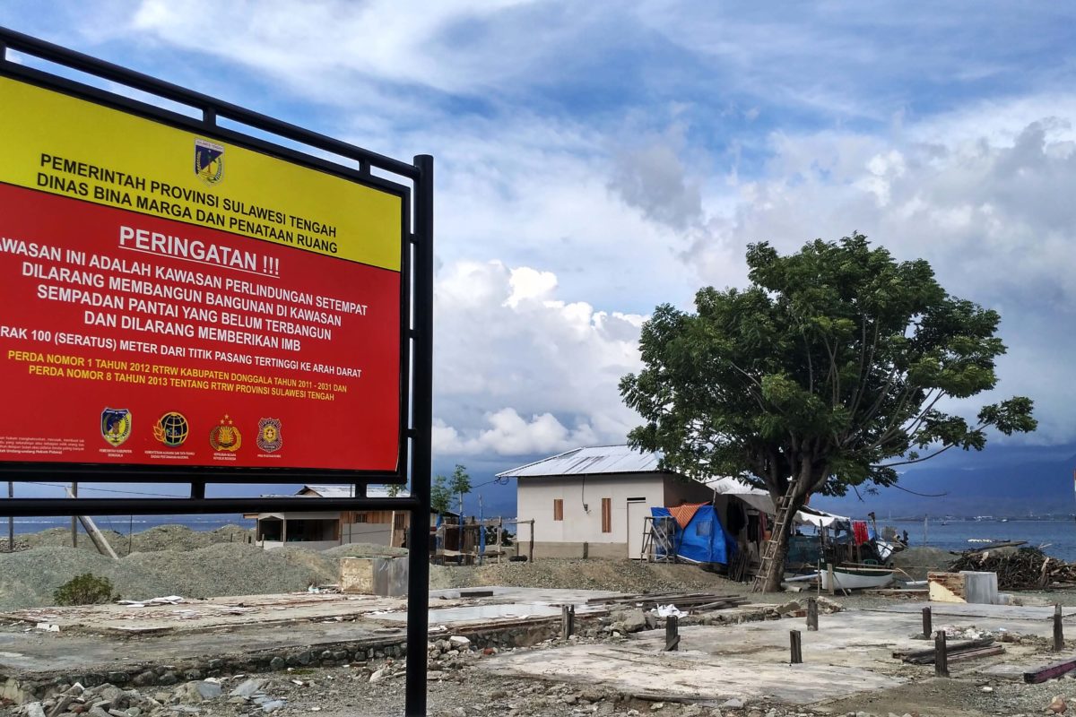 Papan pengumuman berlatar rumah Nana hunia sementaradari puing rumahnya yang hancur di hantam tsunami. Foto: Rosmini 2020