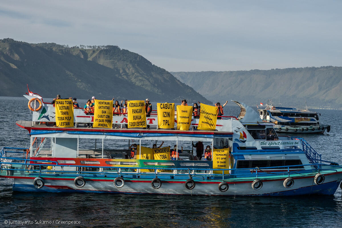 Para aktivis dan peremouan adat memegang poster di dalam kapal ferry di tengah Danau Toba. Foto: Greenpeace Indonesia